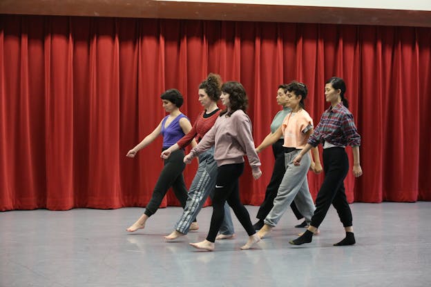 Six performers walk aligned with three in the front and three in the back. Their right hand goes forward while the left leg leads.