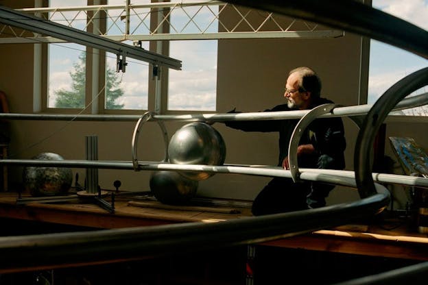 Image of a man touching a big silver sphere, which is supported by a metallic track.