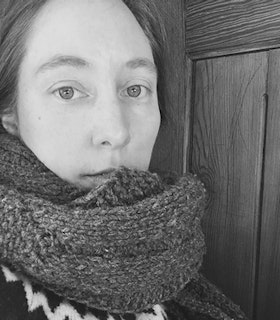 Black and white headshot of Kim Brandt in a sweater and scarf covering their neck and chin.