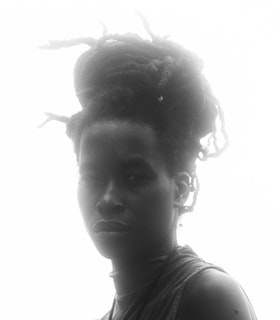 A black and white portrait of Camae Ayewa with strong white light behind her. She wears a sleeveless mock turtleneck and her hair is gathered on a knot to the top.