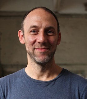 Portrait of David Levine smiling at the camera with a dark blue T-shirt, close cut hair and a short graying beard.
