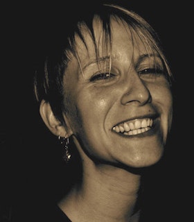 Sepia portriat of Melanie Maar smiling at the camera, with short blonde bangs covering her forehead.