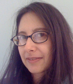 Close up portrait of Melinda Ring smiling at the camera, with ovular glasses and straight brown hair.