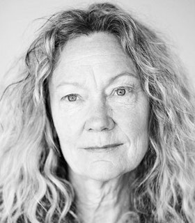 A black and white portrait of Sara Shelton-Mann, slightly smiling at the camera with long, curly, blonde hair.