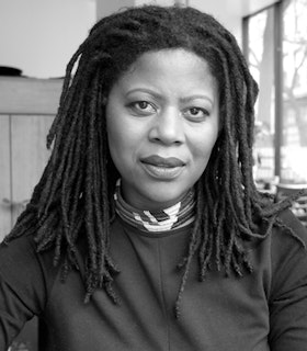 A black and white portrait of Simone Leigh, with her hair locked and wearing a patterned necklace and black top.