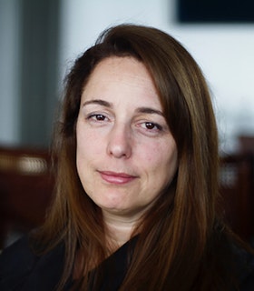 Portrait of Tania Bruguera with midlength brown hair wearing a black long sleeve shirt.