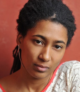 Portrait of Tomeka Reid with black hair, a nose ring and a white flowery top with an orange neckline.