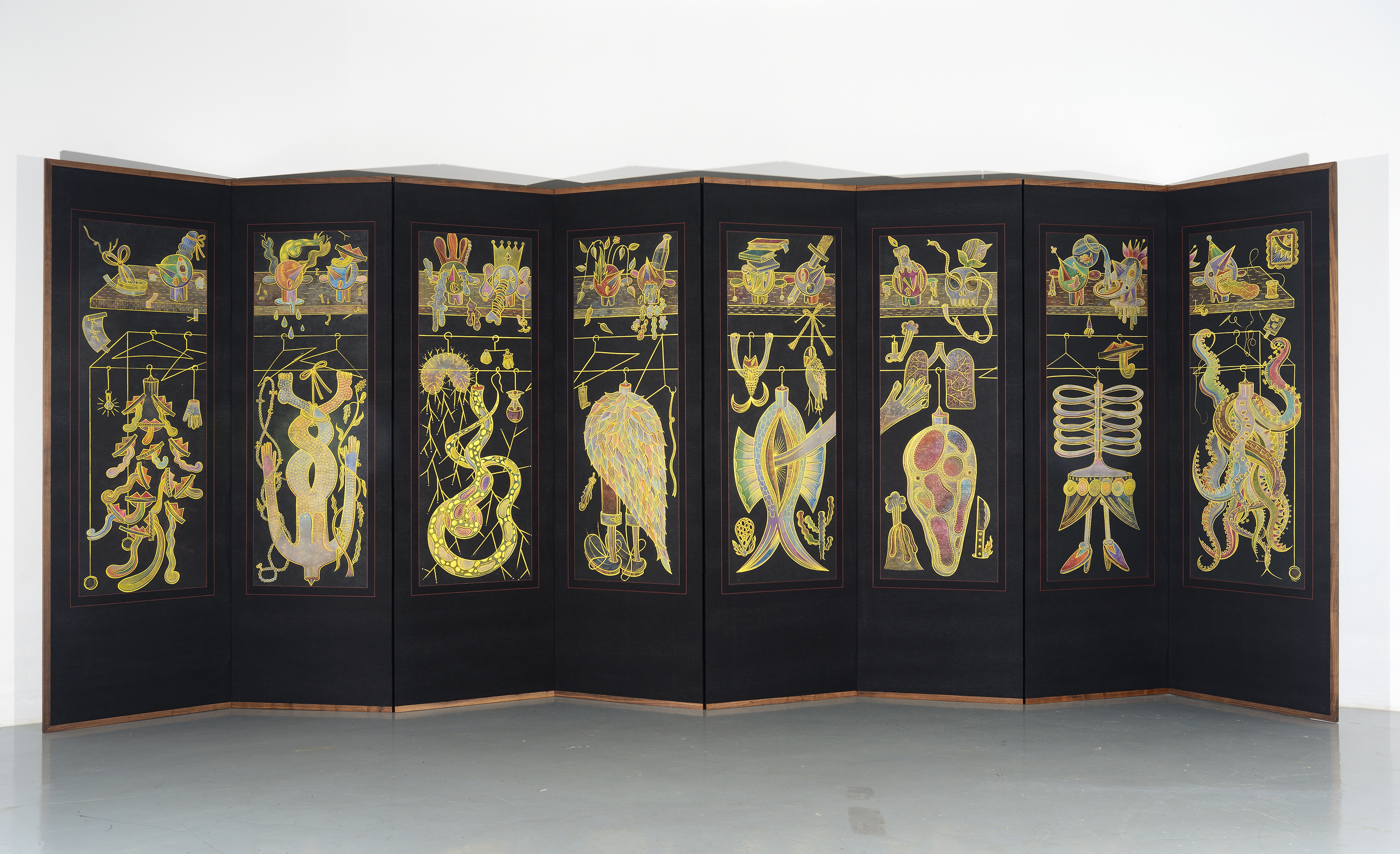 A black, eight-paneled room divider extends across a white-walled. The divider is framed on all sides by a narrow wooden border and each panel depicts an illustration of a colorful and cluttered closet, in which gilded flora, fauna, and hybrid forms hang from golden clothing racks. 