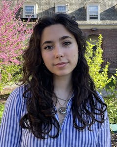 Portrait of Livia Weiner outdoors, looking at the camera, wearing a striped button-down shirt with long brown hair.
