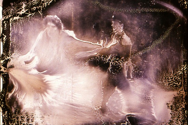 A pink tinted, distorted, video still of two people. The person on the left appears to reach outwards towards the left, beyond the frame of the image. The person on the right meanwhile reaches out their hand toward the person on the left. The image has a metallic quality and there are gold scratches around the border of the scene.