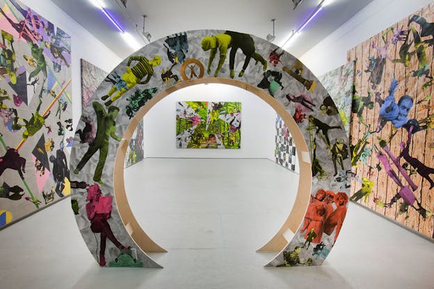 Installation view of a circular arch pasted with collaged technicolor human figures performing various actions against a light gray geometric background. Covering the surrounding walls are large canvases hosting collaged and juxtaposed colorful figures and shapes. 