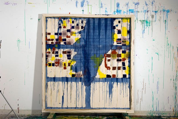 Cream-colored canvas divided into 3x2 rows by blue paint constituting a large irregular smear of grayish blue extending from the upper center and fading at the lower center surrounded by yellow, red, and brown square shapes in the upper two rows and blue paint dripping down the third row, propped against a white wall spattered with dripping blue paint.