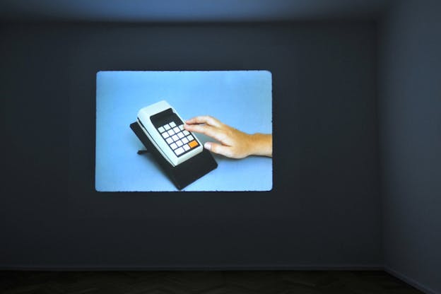 Projection on a dark room's wall depicting a hand reaching towards an electronic device with buttons on a blue background.