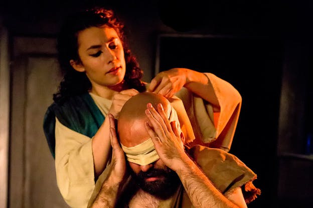 Close-up of a person focused on adjusting the blindfold on a person resting their hands on their temples.