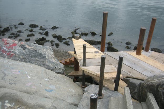 Wooden planks with poles around them situated on a sandy area with rocks underneath the , create a small wharf. 