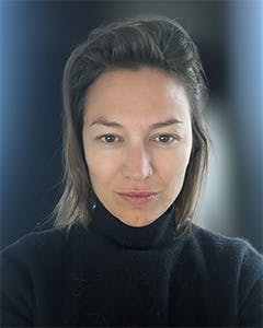 Color portrait of Arantxa looking to the camera. Her hair is just above shoulder length and pushed back. She looks directly into the camera. She is wearing a black turtleneck.