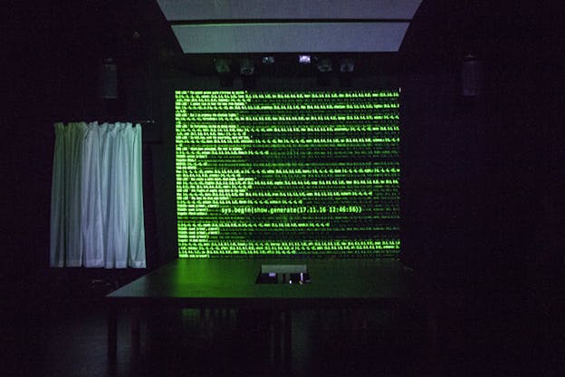 A projection on the wall with green typed sentences behind a back table.