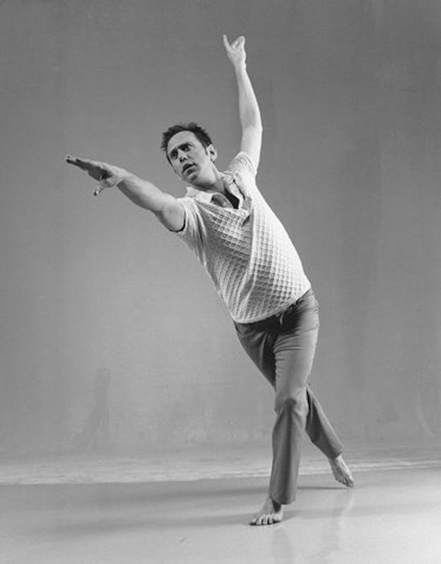 A performer leans forward with their hands turned upwards and one leg in front of the other.