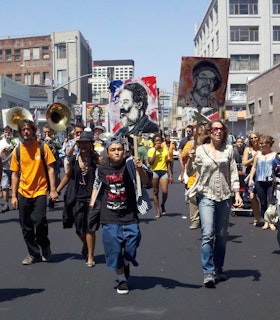 People on the street walk in formation holding up signs with drawn faces on them.