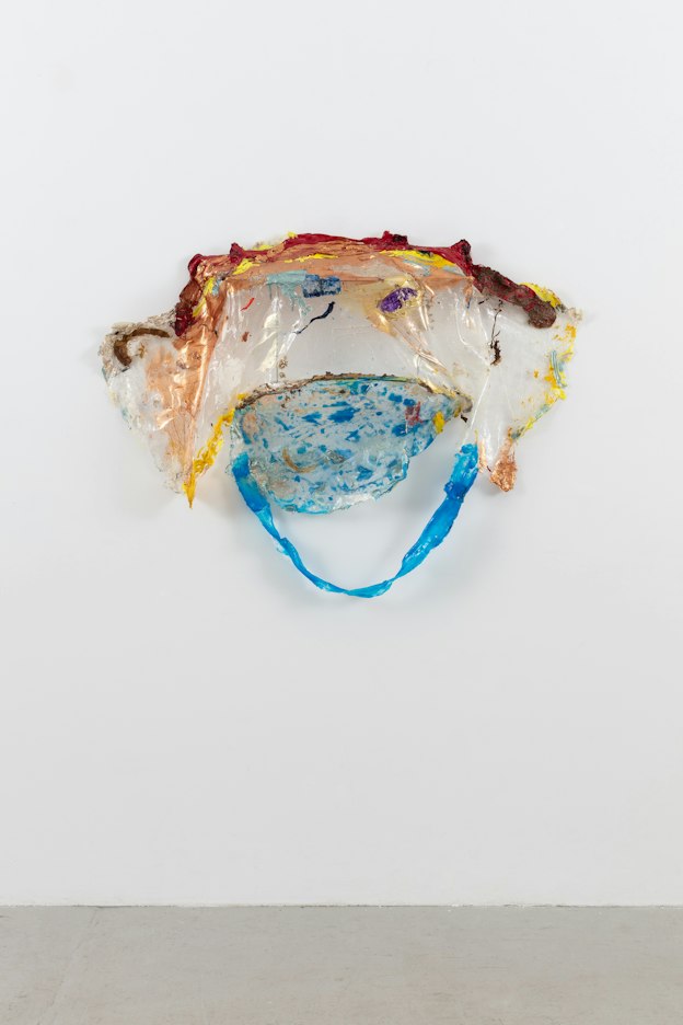 A sculpture made from torn plastic, painted with acrylic paint. The top, painted with rusty red, orange, and yellow, forms a shallow shelf covering a hanging under-section. The texture of the paint on top forms a tendril-like structure, while the under-section drapes mostly unpainted, and transitions into a smaller, round, speckled blue painted component. A strip of painted blue plastic hangs in a loose arc beneath the speckled portion.