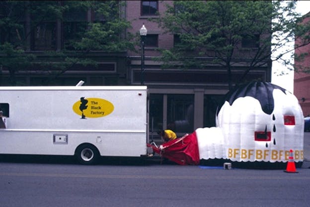 A white truck is parked on a city street. The truck has a yellow sticker on it which reads 