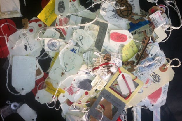 Photograph of a pile of tags cut-out and decorated with ribbons and drawings. 