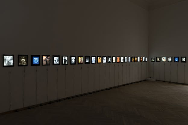 Aligned lightboxes depicting various images situated on two walls and connected each by cables going straight to the floor.