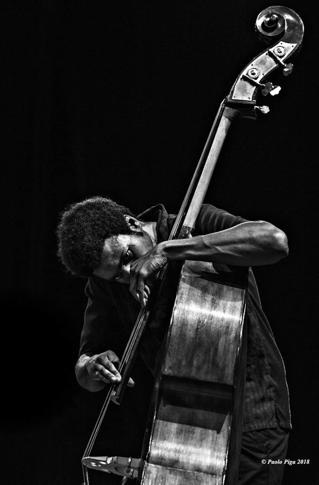 A black and white image of Luke Stewart. His head is down while he plays the upright bass.