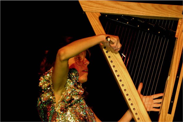 A person dressed in a glittery top plays a string instrument by holding a wandlike object in their hand.