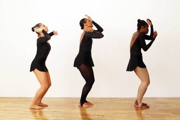 Three dancers aligned, bending and contracting, raising their hands towards their faces.