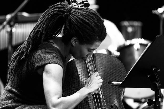 Black and white portrait of Tomeka Reid holding in front of them and playing a cello.