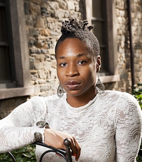 Portrait of Marjani Forté-Saunders seated backwards on a chair, dressed in a white lace shirt.