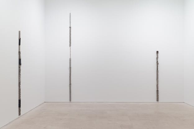 Three lines of different lengths on two white walls. They are made of a metallic material that has been bended in different section of the length in various patterns.