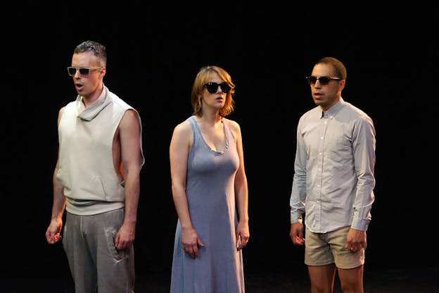 A video still of My Barbarian preforming against a black background. They each wear sunglasses and stand with their arms at their sides, mouths slightly open, facing different directions. On the left, Alexandro Segade stands wearing a white sleeves less turtleneck and grey sweat pants. In the middle, Jade Gordon stands wearing a blue dress. Malik Gaines stands on the rigth wearing khaki shorts and a light blue button up.