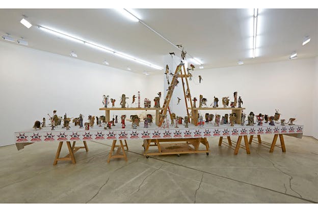 An installation of small aligned figurines with a wooden ladder in the middle stands on top of a table.  