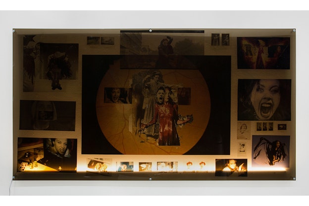 Images on a wall showcase various figures and faces screaming. In the center of them all, a collage of an eye covered by screaming faces and a bloodied figures.