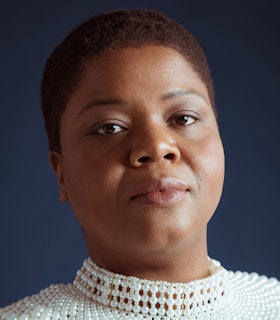 A portrait of Lisa E. Harris with cropped dark-auburn hair wearing a mock neck top sewn of white pearls.