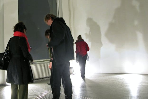 A performance image of the grey room with strings filled with audience members who walk on top of the strings and peer down at them. 