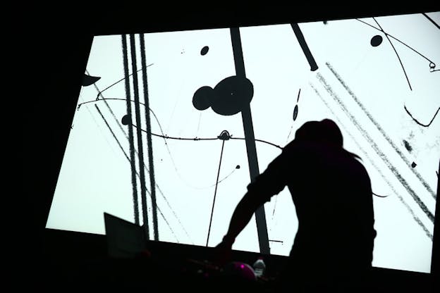 Silhouette of a person in front of a computer and cables in front of a projection of a white background with black lines and circles.