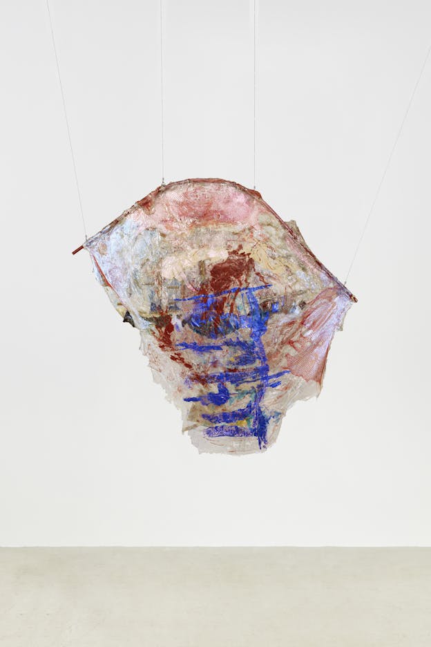 A hanging sculpture made of draped material over an arced rod. The material has a slightly opalescent sheen, and areas of red paint towards the top, with darker abstract forms painted towards the bottom in darker red and deep blue. The bottom edge of the material is torn.