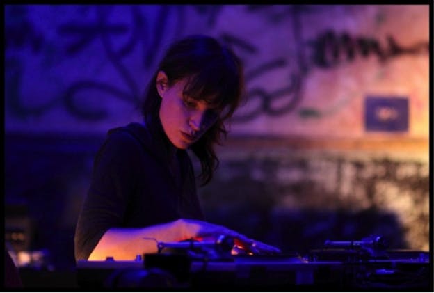Close-up of Rosenfeld concentraing on DJing in a room hued with fuschia and violet light. 