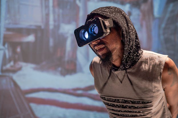 A person a gray and black hooded shirt, wearing VR goggles.