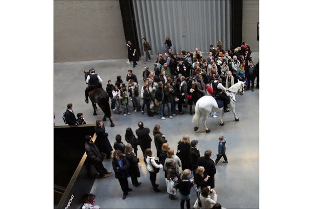 A crowd separates in two sides to open space for two horsemen on white and black horses as they go on opposite directions.