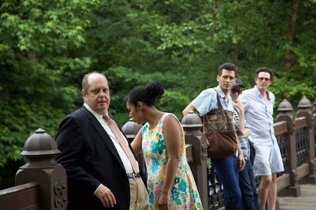 Two people in the front closest to the viewer stand together, with one of them looking over the bridge and the other looking towards the distance. Three others further away look at the same distance direction. 