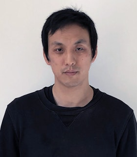 A portrait of Ian Cheng with cropped dark hair, wearing a black t-shirt.