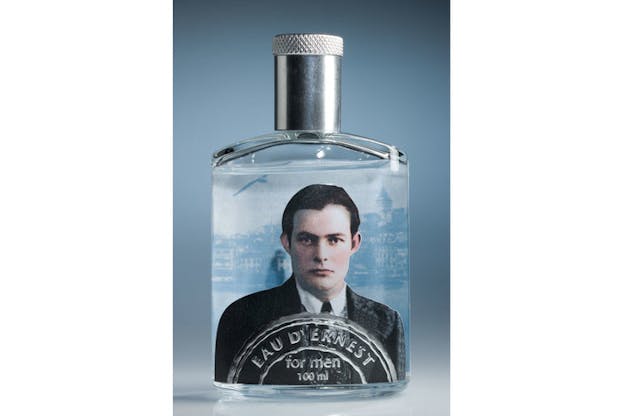 Close-up of a cologne bottle pasted with a color photograph of young Ernest Hemingway and the description: 