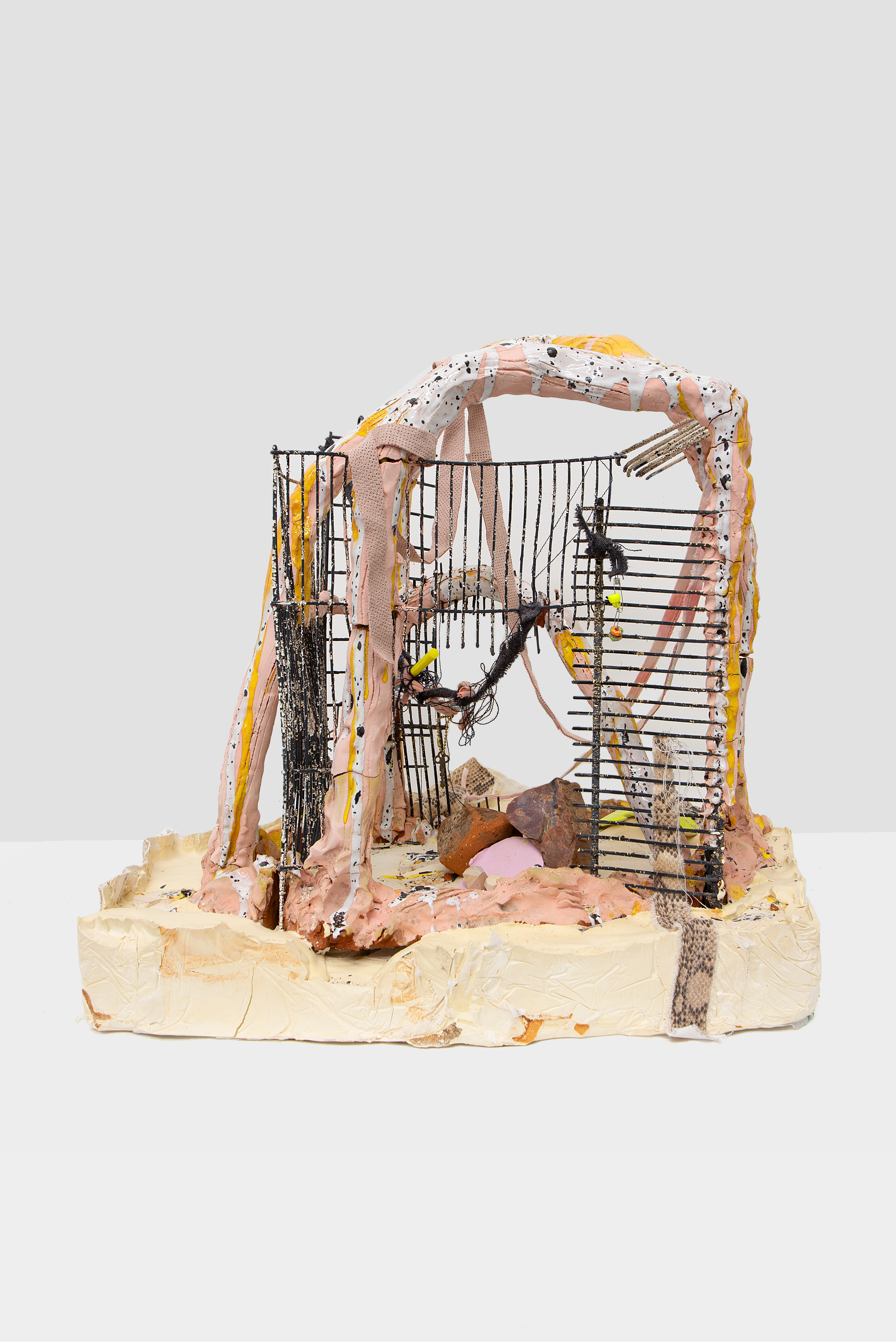 A ceramic sculpture comprised of salmon pink, white, tan, and orange arches embedded with metal grating on a thick clay base.