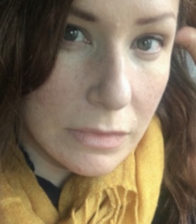 Close up portrait of Anne Boyer with brown straight hair, a side swept bang and green eyes, wearing a yellow scarf.