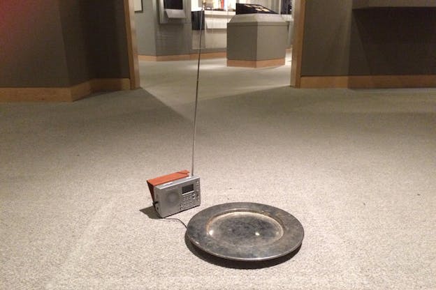 A metallic plate on the floor connected to an old school radio with a long antenna through a cable.
