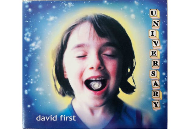 A close up image of a child shows them closing their eyes and opening their mouth. In the inside of their mouth, an image of a small silver galaxy can be seen. A blurred yellow circle is behind their head. The rest of the background is shades of blue with spots of white. In the bottom left corner, it says 